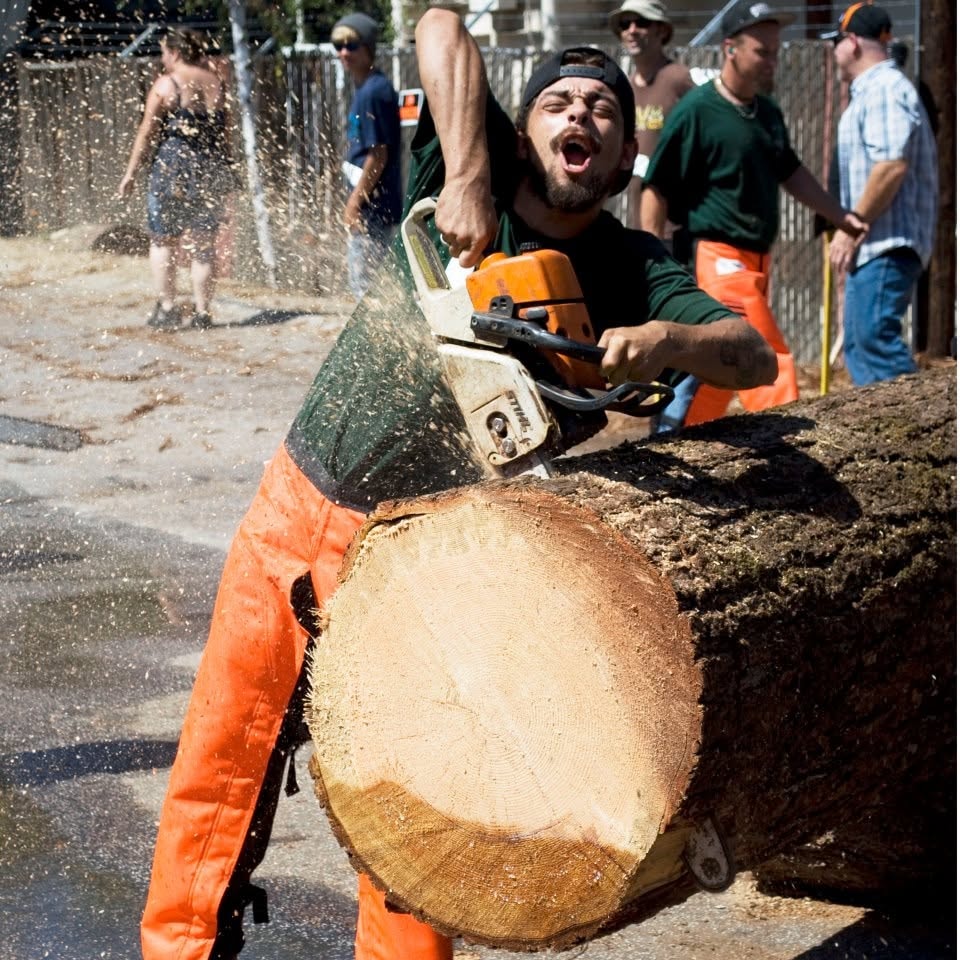 Caleb Armstrong cutting a log with a chainsaw during a local timber event